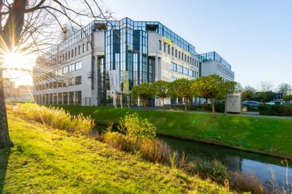 Kantoorgebouw aan de De Bruyn Kopsstraat met moderne gevel, glaspartijen en omliggend groen met een waterloop.